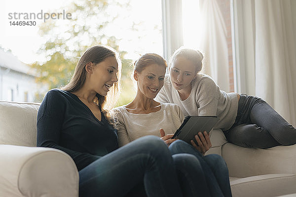 Glückliche Mutter mit zwei Mädchen im Teenageralter  die zu Hause Tabletten auf der Couch benutzen