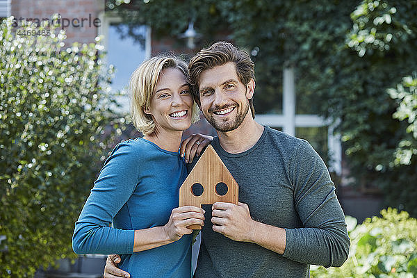 Porträt eines glücklichen Paares vor ihrem Haus mit Hausmodell