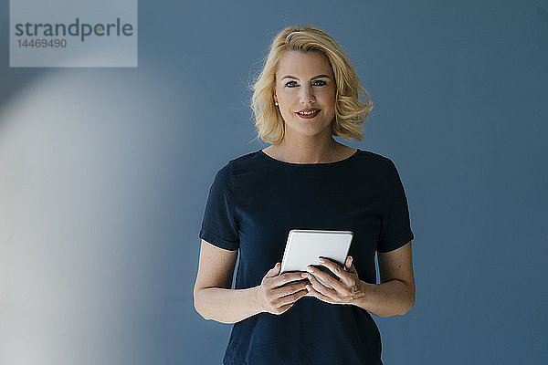 Porträt einer lächelnden blonden Frau mit Tablette in der Hand