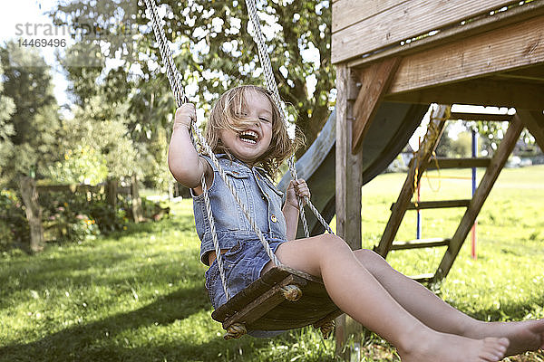 Lachendes kleines Mädchen sitzt auf einer Schaukel im Garten