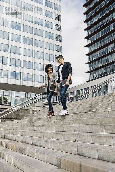 Zwei Kollegen gehen und sprechen auf einer Treppe vor einem Bürogebäude in der Stadt