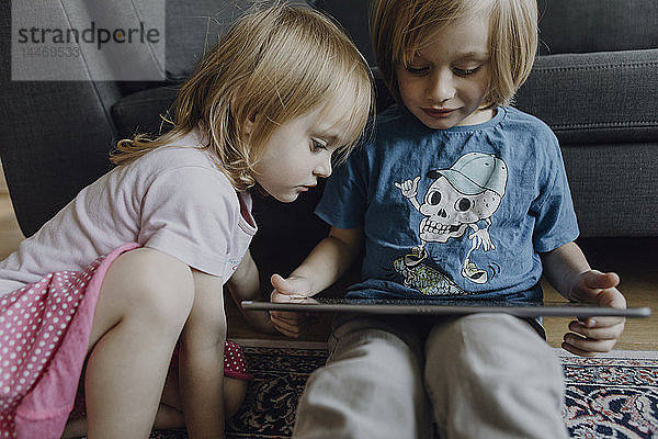 Bruder und kleine Schwester sitzen zu Hause auf dem Boden und benutzen ein digitales Tablett