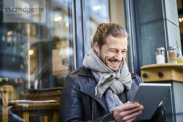 Porträt eines lachenden jungen Mannes vor einem Café  der auf ein Tablett schaut