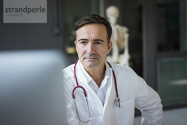 Arzt in medizinischer Praxis betrachtet Computer mit Skelett im Hintergrund