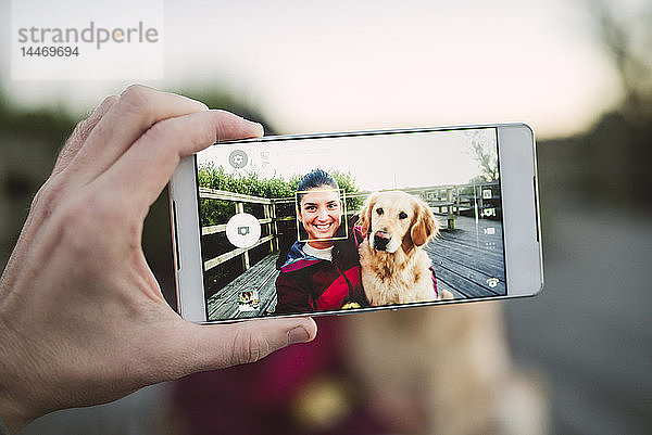 Handy-Bild einer glücklichen jungen Frau mit ihrem Golden-Retriever-Hund im Freien