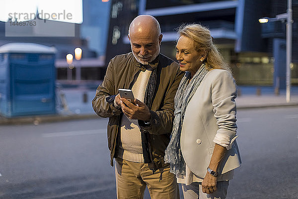 Spanien  Barcelona  älteres Ehepaar  das sich in der Stadt in der Abenddämmerung ein Handy teilt