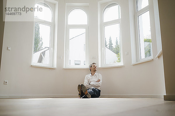 Geschäftsmann sitzt auf dem Boden seines frisch renovierten Hauses und sieht glücklich aus