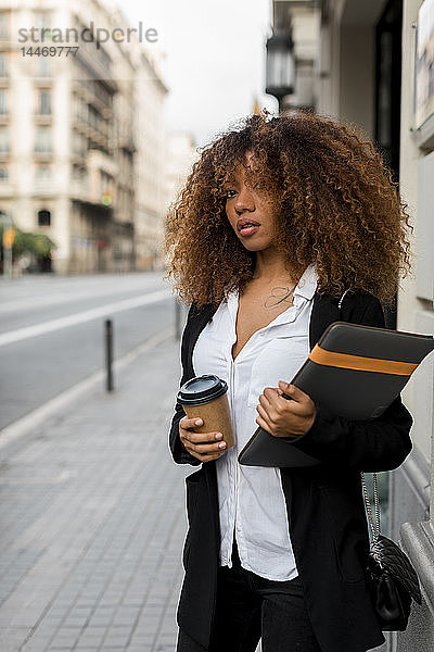 Junge Frau mit Laptoptasche und Kaffee zum Mitnehmen in der Stadt