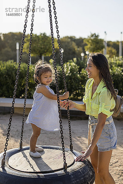 Glückliche Mutter mit Tochter auf Reifenschaukel auf einem Spielplatz