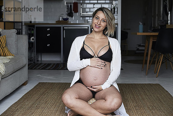 Porträt einer lächelnden  blonden  schwangeren Frau  die zu Hause auf dem Boden sitzt
