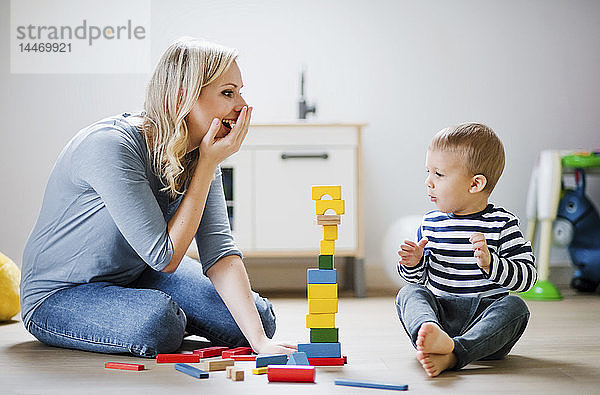 Glückliche Mutter und Kleinkind spielen zu Hause mit Bauklötzen