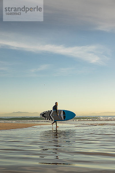 Spanien  Andalusien  Tarifa  Mann geht mit aufrechtem Paddelbrett am Strand