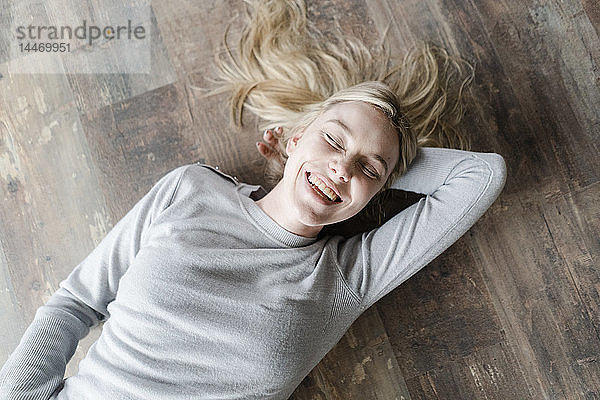 Glückliche blonde junge Frau auf Holzboden liegend