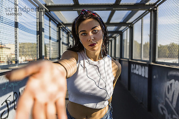 Porträt einer jungen Frau mit Ohrstöpseln auf einer Brücke  die ihre Hand ausstreckt