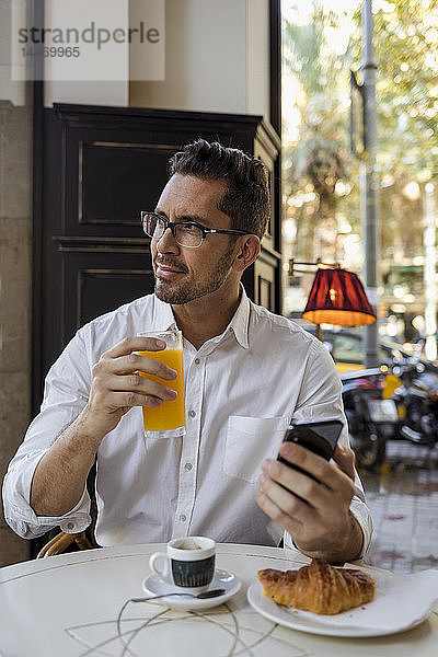 Geschäftsmann beim Frühstück in einem Café mit Handy in der Hand