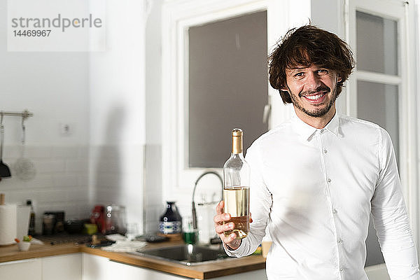 Mann steht in der Küche und hält eine Flasche Weißwein