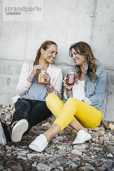 Zwei Freundinnen trinken Smoothies im Freien und amüsieren sich