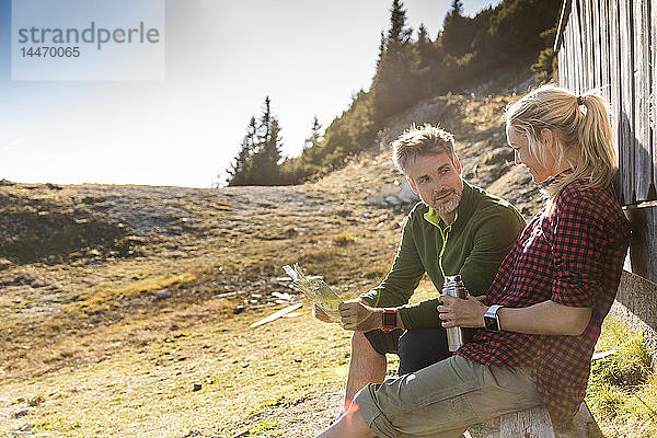 Wandererpaar sitzt vor der Berghütte  macht Pause  hält Karte