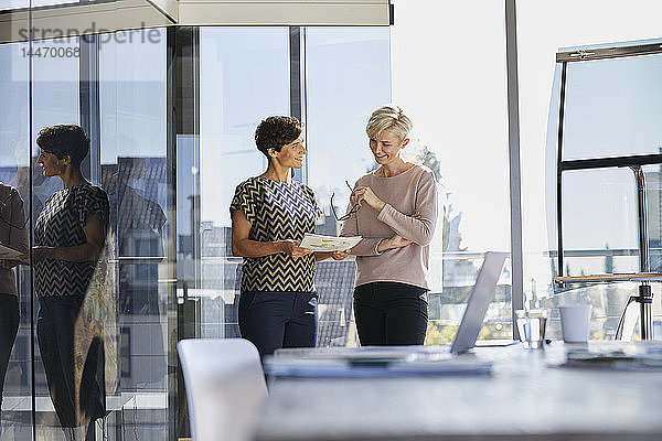 Zwei lächelnde Geschäftsfrauen diskutieren am Fenster im Büro über ein Dokument