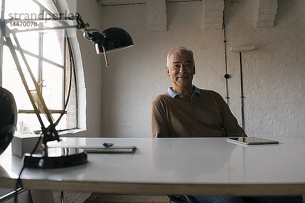 Porträt eines lächelnden älteren Geschäftsmannes am Schreibtisch sitzend im Büro