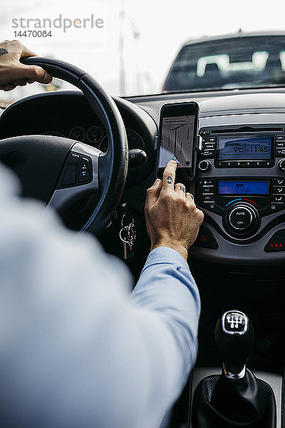 Nahaufnahme eines Mannes mit tätowierter Hand beim Autofahren mit einem Mobiltelefon als Navigationssystem