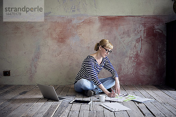 Frau sitzt auf Holzboden in einem unrenovierten Zimmer eines Dachgeschosses und arbeitet
