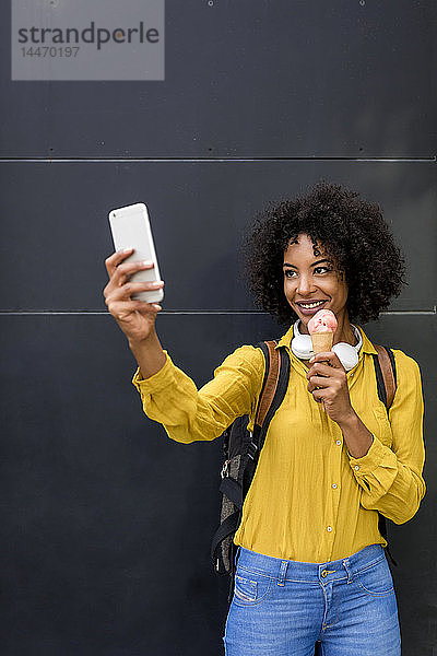 Porträt einer lächelnden Frau mit Eistüte  die sich mit einem Smartphone selbstständig macht