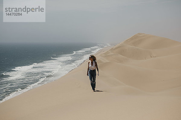 Namibia  Walvis Bay  Namib-Naukluft-Nationalpark  Sandwich-Hafen  Frau wandert in Dünenlandschaft am Meer