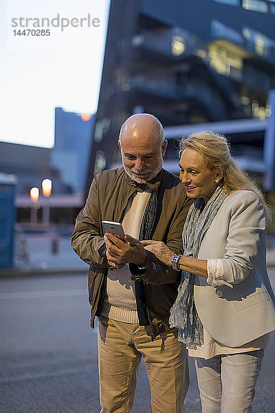 Spanien  Barcelona  älteres Ehepaar  das sich in der Stadt in der Abenddämmerung ein Handy teilt