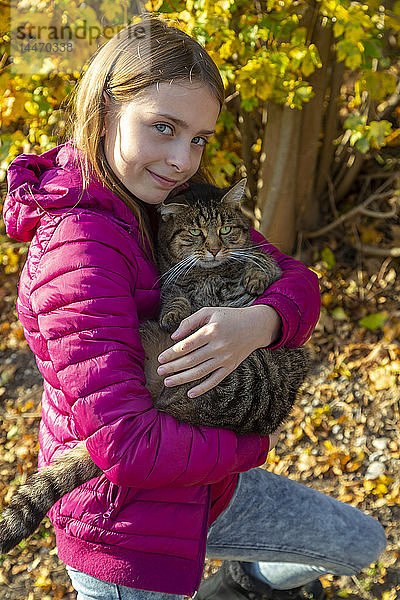 Porträt eines lächelnden Mädchens  das im Herbst eine gestromte Katze im Freien hält