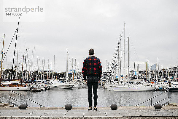Rückenansicht eines jungen Mannes in legerer Kleidung beim Blick auf den Hafen