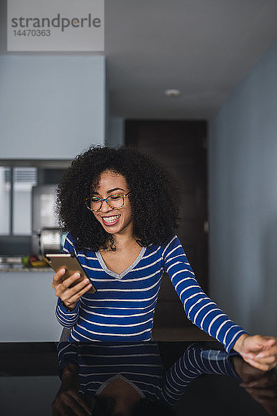 Porträt einer glücklichen jungen Frau  die zu Hause auf ihr Handy schaut
