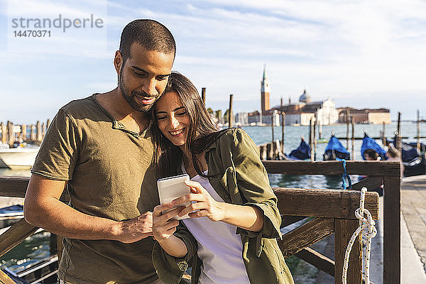 Italien  Venedig  liebevolles junges Paar mit Handy und Gondelbooten im Hintergrund