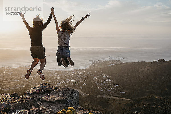 Südafrika  Kapstadt  Kloof Nek  zwei Frauen springen bei Sonnenuntergang auf Felsen