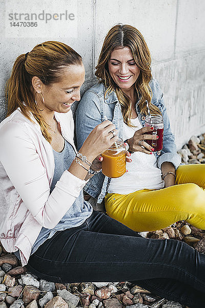 Zwei Freundinnen trinken Smoothies im Freien und amüsieren sich