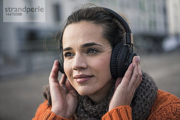 Porträt einer lächelnden Frau  die im Herbst mit schnurlosen Kopfhörern Musik hört