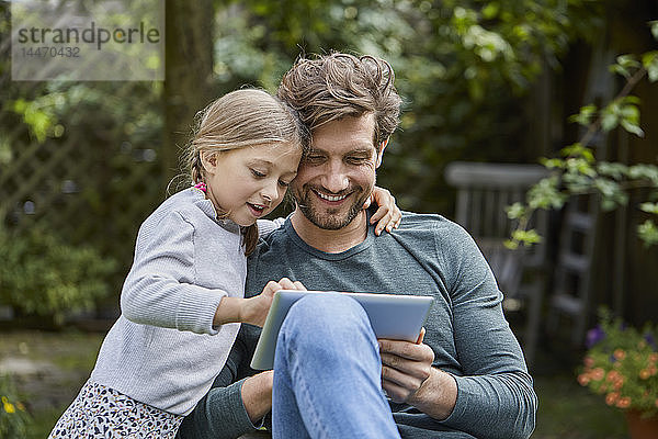 Glücklicher Vater und Tochter benutzen gemeinsam Tablette im Garten