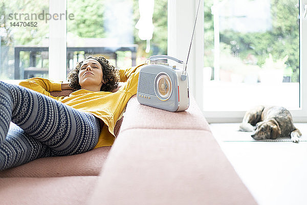 Frau liegt auf dem Sofa und hört zu Hause Musik mit einem tragbaren Radio