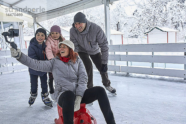 Familie mit zwei Kindern auf der Eislaufbahn  die sich mit ihrem Smartphone selbst mitnehmen