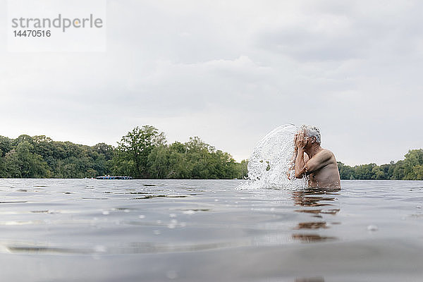 Älterer Mann in einem See  der ihm Wasser ins Gesicht spritzt