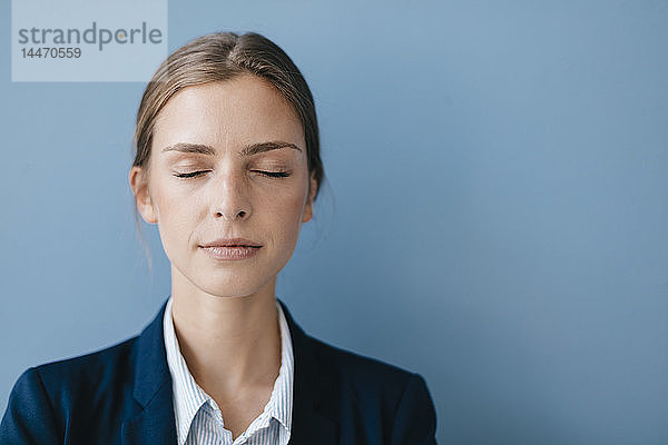 Porträt einer jungen Geschäftsfrau vor blauem Hintergrund  die sich mit geschlossenen Augen entspannt