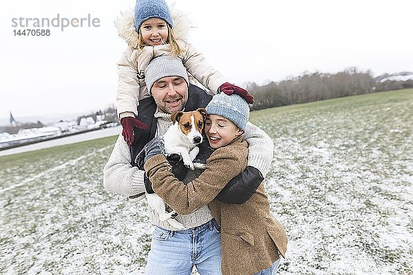 Glücklicher Vater mit zwei Kindern und Hund in Winterlandschaft