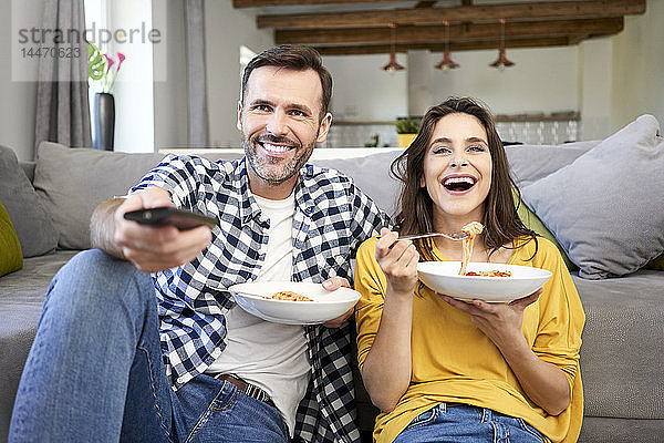 Ehepaar sitzt im Wohnzimmer  isst Spaghetti und sieht fern