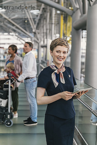 Porträt eines lächelnden Mitarbeiters einer Fluggesellschaft  der auf dem Flughafen eine Tablette in der Hand hält