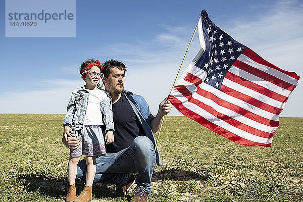 Mann mit Tochter und amerikanischer Flagge auf Feld in entlegener Landschaft