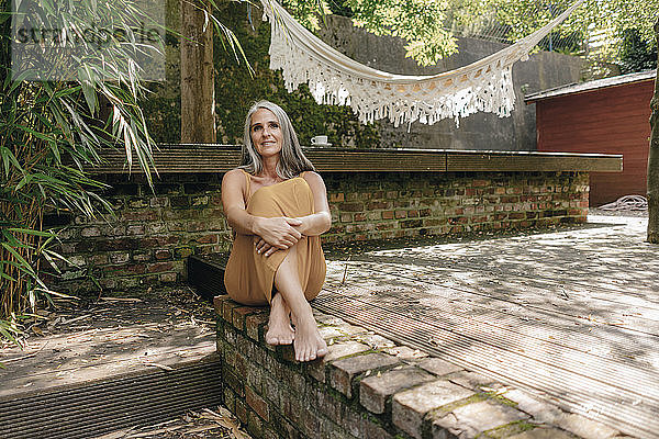 Porträt einer lächelnden Frau  die barfuss auf der Terrasse im Hinterhof sitzt