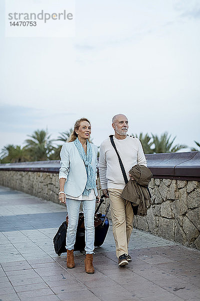 Spanien  Barcelona  Seniorenpaar geht mit Gepäck auf der Promenade