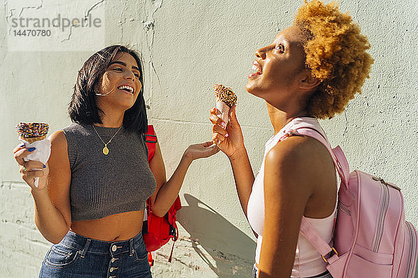 Zwei glückliche Freundinnen mit Eistüten an einer Wand