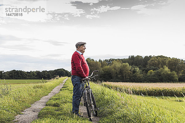 Älterer Mann mit Fahrrad in ländlicher Landschaft