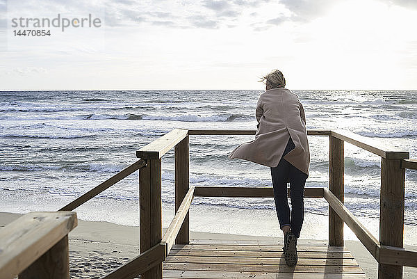 Spanien  Menorca  Rückenansicht einer älteren Frau  die im Winter auf einer Strandpromenade steht und auf das Meer schaut